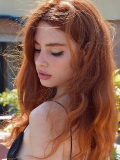 Woman with long red hair and freckles looking down, with exposed shoulder