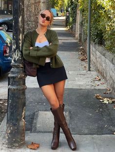Woman in a green cardigan and mini skirt posing on a sidewalk