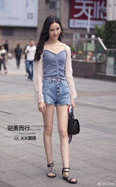 Woman with long dark hair wearing denim shorts and a sheer top on a street
