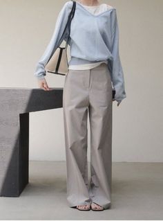 Person in light blue sweater and wide leg pants holding a shoulder bag