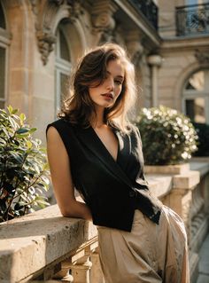 Woman with long hair wearing a black vest and khaki pants on a balcony