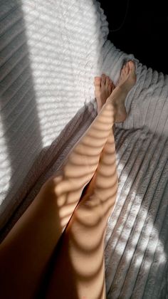 Bare legs with shadows from blinds on a textured blanket