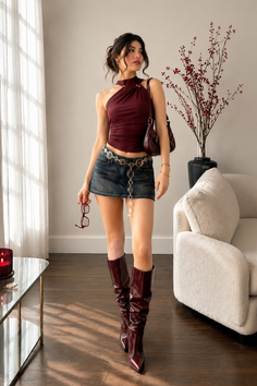 Woman in a denim mini skirt and halter top with knee high boots indoors