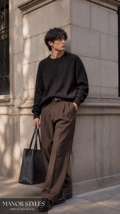 Man in a black sweater and brown pants holding a black tote bag outdoors