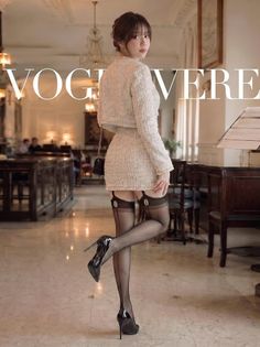 Woman in a tweed suit, stockings, and high heels posing indoors