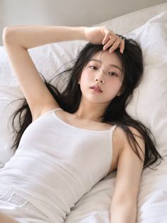 Woman with long black hair in a white tank top lying on a bed