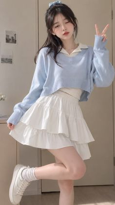 Woman in a blue sweater and white tiered skirt posing indoors