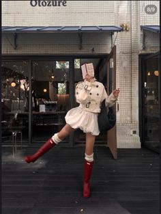 Person in a white trench coat and red boots posing outside a cafe