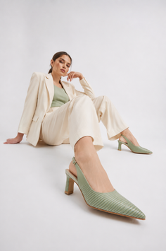 Woman in a cream suit and green top sitting on a white studio floor