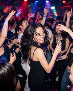 Woman in a black dress holding a champagne glass at a lively nightclub