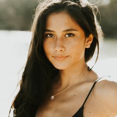 Woman with long dark hair and freckles wearing a black top and shell necklace