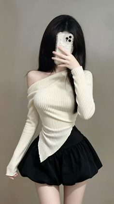 Woman with long black hair taking a mirror selfie in an off-shoulder top and mini skirt
