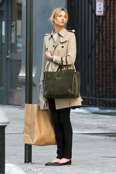 Woman in a trench coat holding a large bag and shopping bag on a street
