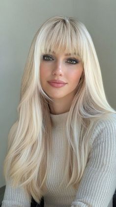 Woman with long blonde hair and bangs wearing a light-colored turtleneck sweater