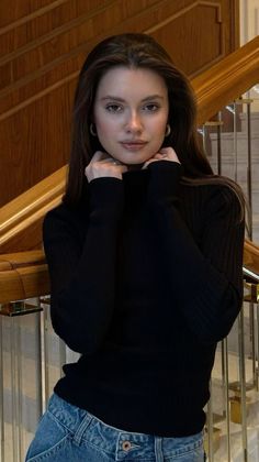 Woman with long brown hair wearing a black turtleneck and jeans indoors