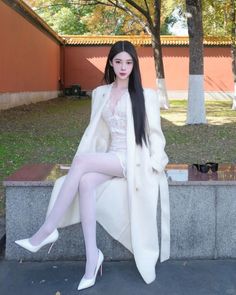 Woman with long black hair wearing a white coat and lace dress outdoors