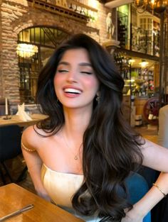 Woman with long dark hair wearing a strapless top and pearl necklace, smiling in a restaurant