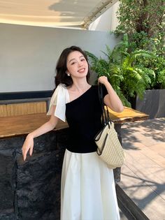 Woman in a black one-shoulder top and white skirt holding a straw bag outdoors