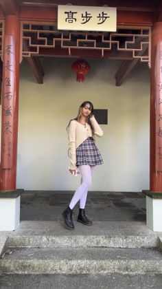 Woman in a plaid skirt and white tights standing in an outdoor Asian-style structure