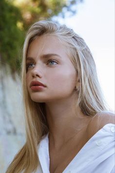 Young woman with blonde hair and blue eyes wearing a white shirt outdoors