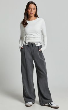 Woman in a white long sleeve shirt and gray wide leg pants with hands in pockets