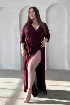 Woman in a maroon dress with a high slit and cleavage, posing indoors