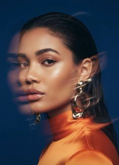 Woman with slicked-back hair and large earrings against a dark background