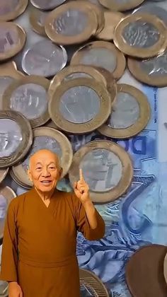 Monk in a brown robe pointing upwards, with coins and currency in the background