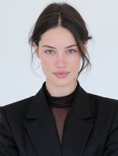 Woman with dark hair wearing a black blazer and sheer top against a white background