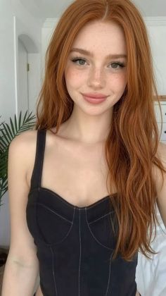 Woman with long red hair and freckles wearing a black top indoors