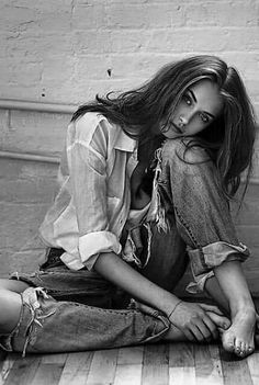 Woman with long hair and ripped jeans sitting barefoot on a wooden floor