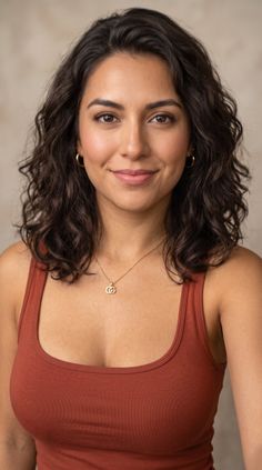 Woman with wavy brown hair wearing a brown top and gold jewelry