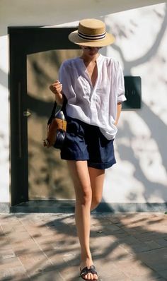 Woman in a straw hat, white shirt, and denim shorts walking outdoors