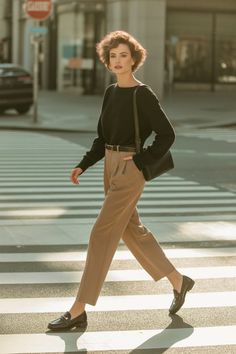 Woman with short hair in a black sweater and khaki pants crossing a city street