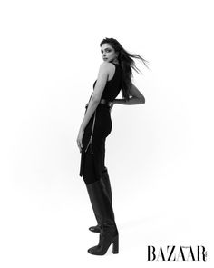 Woman in a black dress and knee-high boots posing in a studio