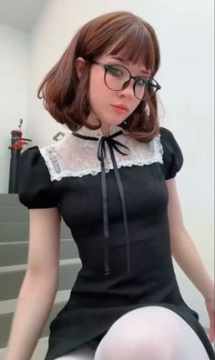 Woman with short brown hair and glasses wearing a black dress with white lace