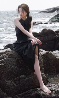 Woman in a black dress sitting on rocks by the ocean