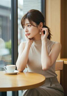 Woman with a ponytail and pearl earrings sitting at a cafe table with a coffee cup