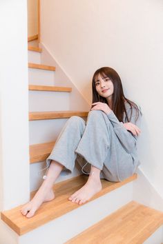 Woman with long hair in gray loungewear sitting barefoot on wooden stairs