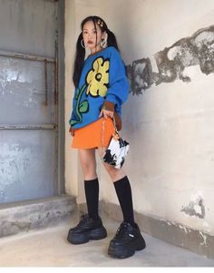 Woman in a blue sweatshirt and orange skirt with pigtails and platform shoes