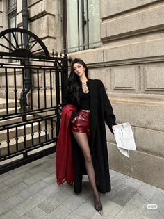 Woman in a black top, red shorts, and long black coat posing outdoors