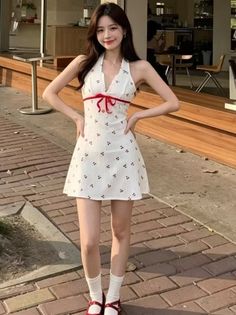 Woman in a white cherry print dress with a red ribbon outdoors