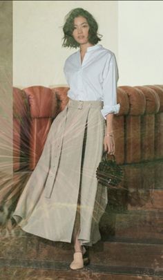 Woman with short hair wearing a white shirt and long skirt, holding a handbag
