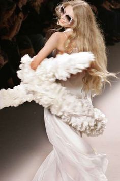 Woman with long blonde hair and sunglasses wearing a white dress and ruffled boa
