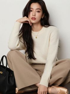 Woman with long dark hair wearing a cream sweater and wide leg pants