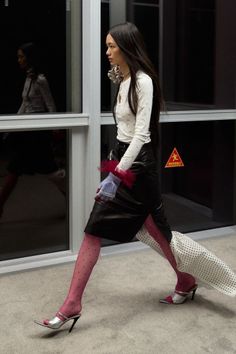 Woman in a leather skirt and pink polka dot tights walking indoors