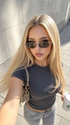 Woman with long blonde hair and sunglasses taking a selfie outdoors