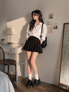 Woman in a white shirt and black pleated skirt standing indoors with soft lighting