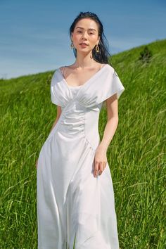 Woman in a white dress standing in a green field under a blue sky