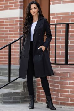 Woman in a black trench coat and black pants standing outdoors